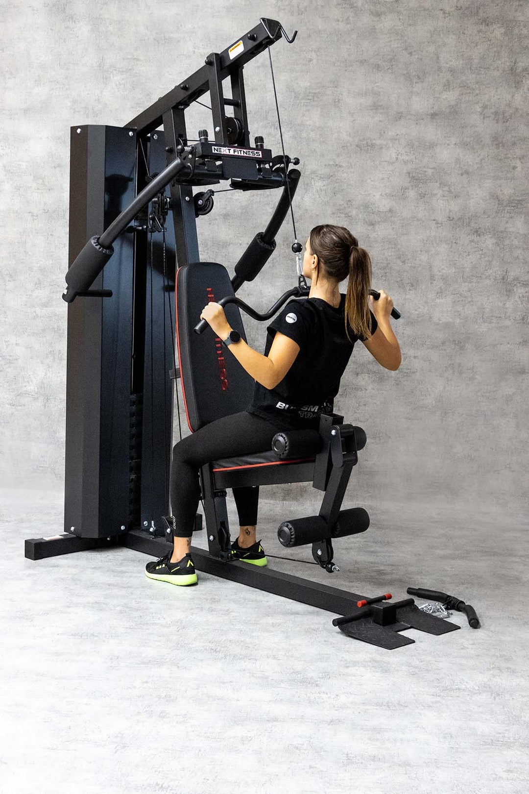 Woman using a multi-station home gym machine performing a lat pulldown exercise, showcasing strength training equipment for full-body workouts in a home gym setup.