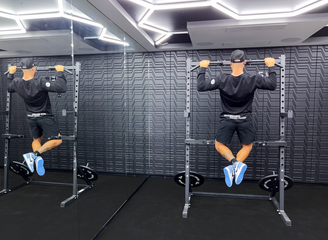 Man performing pull-ups on a power rack in a modern gym, showcasing upper body strength training and home gym equipment setup with mirrored wall and lighting.