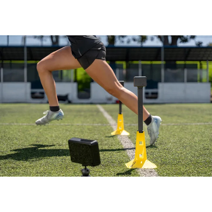 Person running through a series of yellow and black training cones on a sports field.